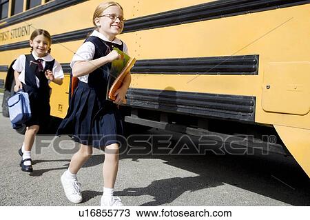 Stock Image - Two schoolgirls running for the school bus. Fotosearch