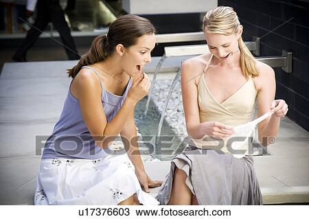 Stock Image - Two women sitting outside laughing at sexy underwear they've just purchased. Fotosearch
