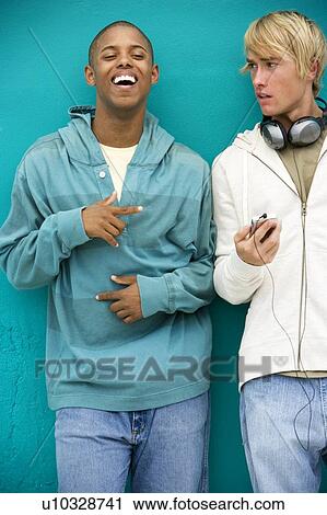 Two young men looking at an MP3 Player leaning against a green painted wall View Large Photo Image Stock Image - Two young men looking at an MP3 Player leaning against a green painted wall . Fotosearch