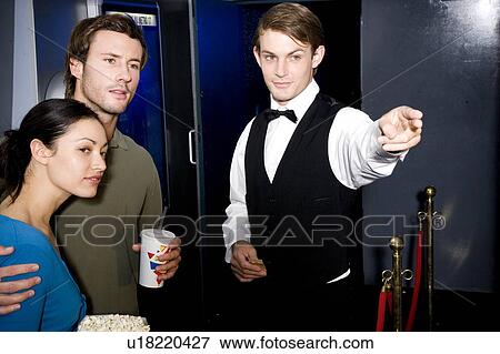 Usher directing young couple at the cinema or theatre View Large Photo Image Stock Photo - Usher directing young couple at the cinema or theatre. Fotosearch
