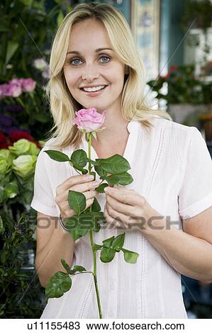Stock Image - Woman florist in her shop, holding a pink rose. Fotosearch