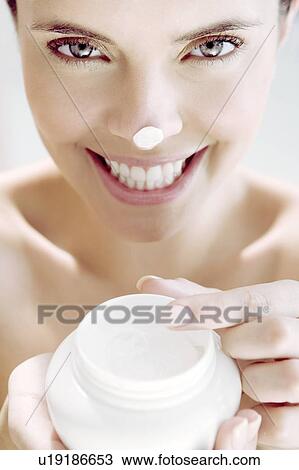 Stock Image - Woman holding a pot of moisturising cream, a blob on her nose. Fotosearch