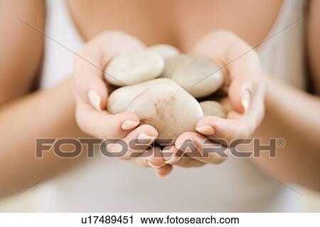 Stock Image - Woman holding stones for hot stone therapy. Fotosearch