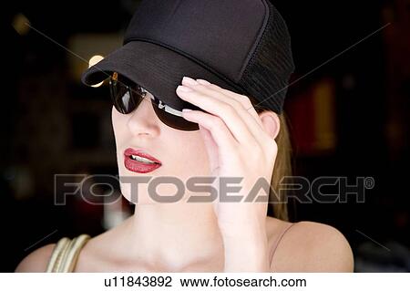 Stock Image - Woman in a baseball cap and sunglasses outdoors. Fotosearch