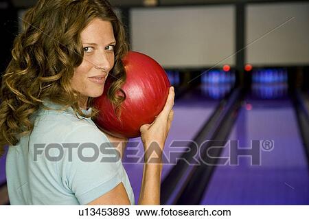 Stock Image - Woman in a bowling alley, holding a red bowling ball. Fotosearch