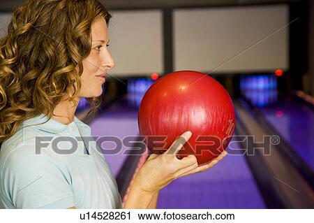 Stock Image - Woman in a bowling alley, holding a red bowling ball. Fotosearch