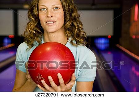 Stock Image - Woman in a bowling alley, holding a red bowling ball. Fotosearch