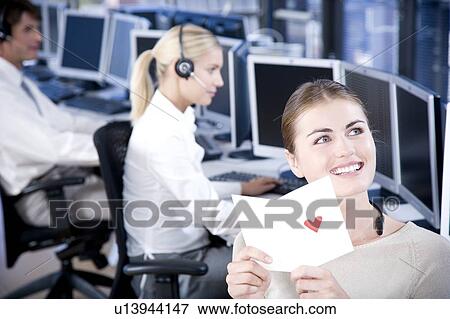 Stock Photo - Woman in a call centre smiling as she opens a Valentines card.. Fotosearch