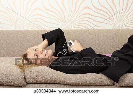 Woman in suit laying on sofa listening to music View Large Photo Image Picture - Woman in suit laying on sofa listening to music. Fotosearch