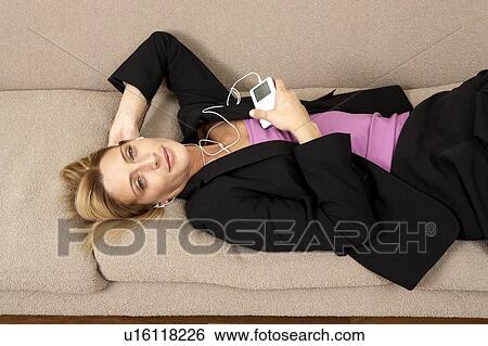 Stock Photograph - Woman in suit laying on sofa listening to music. Fotosearch