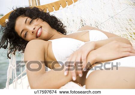 Woman lying in a hammock on a boat in the sun, wearing a white bikini View Large Photo Image Picture - Woman lying in a hammock on a boat in the sun, wearing a white bikini. Fotosearch