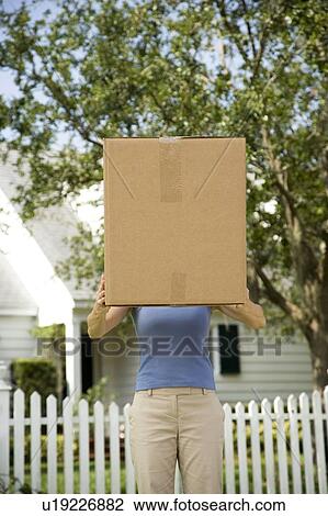 Stock Image - Woman moving house, carrying large packing box. Fotosearch