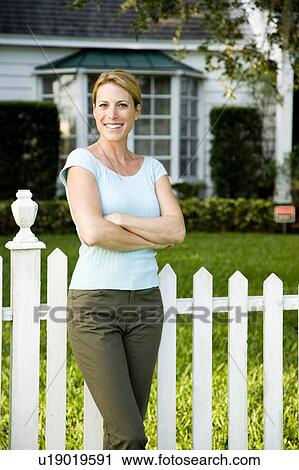 Stock Image - Woman standing by the garden fence outside her new home. Fotosearch