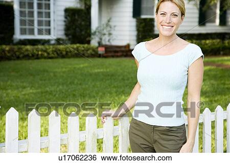 Woman standing by the garden fence outside her new home View Large Photo Image Stock Photograph - Woman standing by the garden fence outside her new home. Fotosearch