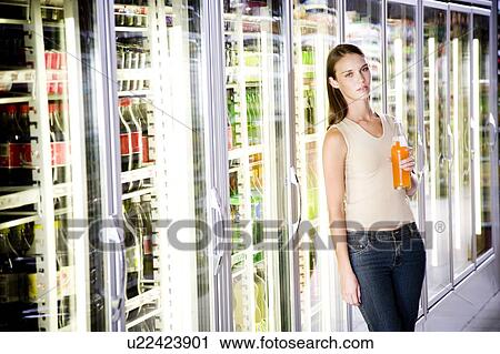 Stock Image - Woman stood next to a refrigerator door in a supermarket. Fotosearch