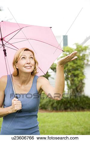 Stock Photograph - woman under umbrella holding out hand to see if still raining. Fotosearch