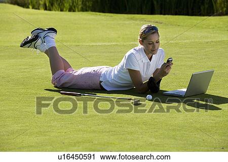 Stock Image - Woman using a laptop and mobile phone whilst on the golf course. Fotosearch