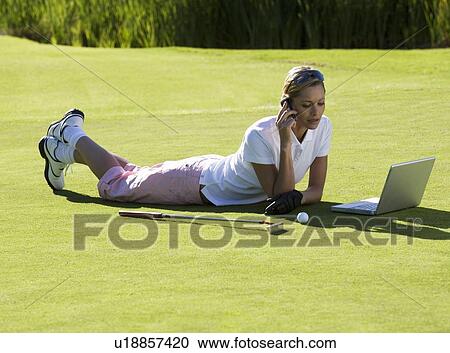 Stock Image - Woman using a laptop and mobile phone whilst on the golf course. Fotosearch