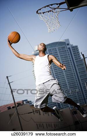 Stock Photo - Young African American man jumping with a basketball on an urban basketball court. Fotosearch