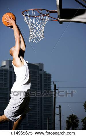 Stock Photography - Young African American man jumping with a basketball on an urban basketball court. Fotosearch