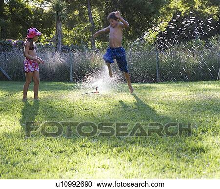 Stock Image - Young boy and girl playing with water in the garden. Fotosearch