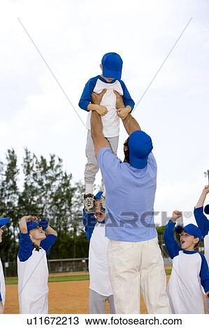 Stock Image - Young boy being lifted up by little league baseball coach. Fotosearch