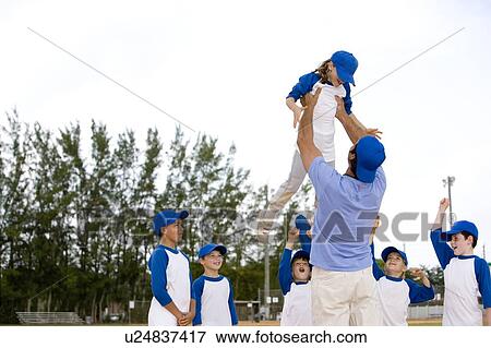 Stock Photo - Young boy being lifted up by little league baseball coach. Fotosearch