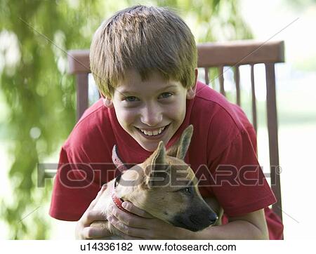 Young boy sitting in a garden chair holding a puppy View Large Photo Image Stock Image - Young boy sitting in a garden chair holding a puppy. Fotosearch