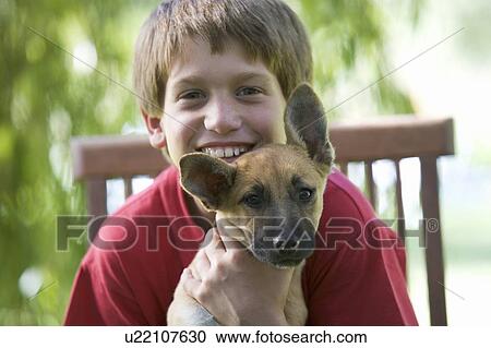 Stock Image - Young boy sitting in a garden chair holding a puppy. Fotosearch
