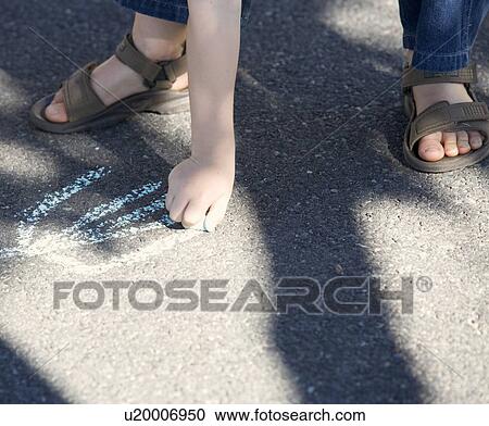 Stock Image - Young boy writing in chalk on the playground, close-up. Fotosearch