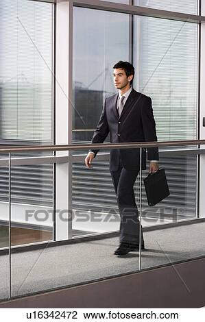 Young businessman in modern office building, walking along with briefcase View Large Photo Image Stock Image - Young businessman in modern office building, walking along with briefcase. Fotosearch