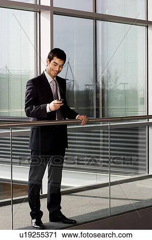 Young businessman in modern office building, checking his mobile phone View Large Photo Image Stock Image - Young businessman in modern office building, checking his mobile phone. Fotosearch