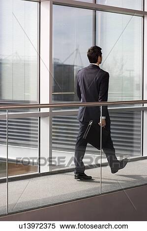 Stock Photography - Young businessman in modern office building, walking along with briefcase. Fotosearch