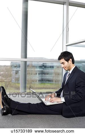 Young businessman sitting on office floor, typing on a laptop View Large Photo Image Stock Photo - Young businessman sitting on office floor, typing on a laptop. Fotosearch