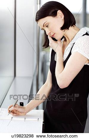 Stock Photo - Young businesswoman or secretary making an appointment in a diary. Fotosearch