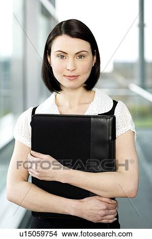 Picture - Young businesswoman standing on office walkway holding folder of papers. Fotosearch