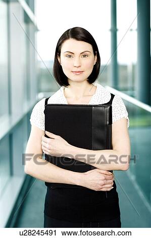 Young businesswoman standing on office walkway holding folder of papers View Large Photo Image Stock Image - Young businesswoman standing on office walkway holding folder of papers. Fotosearch