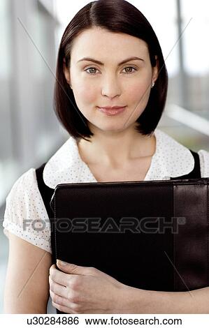 Young businesswoman standing on office walkway holding folder of papers View Large Photo Image Stock Photograph - Young businesswoman standing on office walkway holding folder of papers. Fotosearch