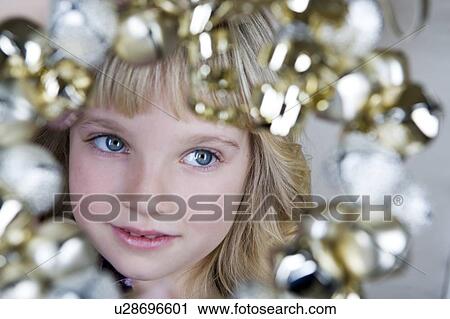 Stock Image - Young girl in a party dress, holding a Christmas decoration . Fotosearch