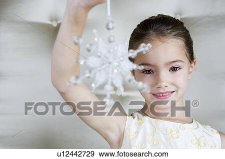 Stock Photo - Young girl in a party dress, holding a Christmas decoration . Fotosearch