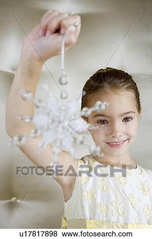 Stock Photo - Young girl in a party dress, holding a Christmas decoration . Fotosearch