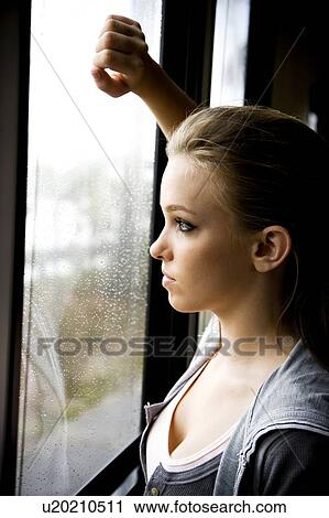 Stock Image - Young girl looking out of a rain covered window . Fotosearch