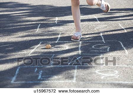 Stock Image - Young girl playing hopscotch. Fotosearch