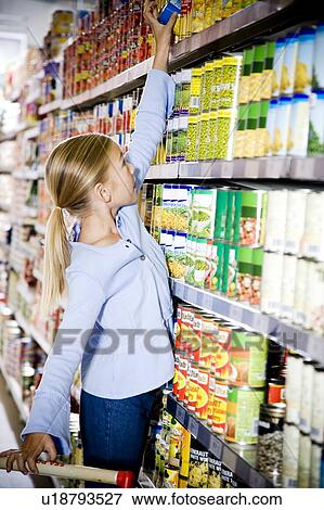 Stock Photo - Young girl reaching up to get something off of a supermarket shelf. Fotosearch
