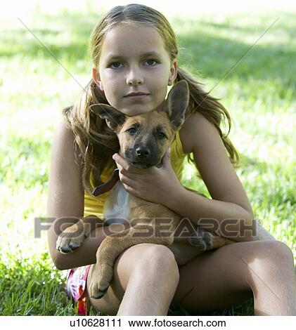 Stock Image - Young girl sitting in the garden holding a puppy. Fotosearch