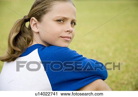 Stock Image - Young girl sitting on the grass looking over her shoulder. Fotosearch