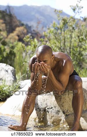 Stock Image - Young man drinking water from cupped hands. Fotosearch