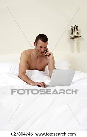 Stock Photography - Young man in bed, working on laptop. Fotosearch