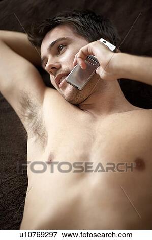 Young man laying on a bed talking on a mobile phone View Large Photo Image Stock Photo - Young man laying on a bed talking on a mobile phone. Fotosearch