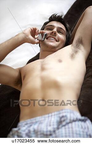 Young man laying on a bed talking on a mobile phone View Large Photo Image Stock Photography - Young man laying on a bed talking on a mobile phone. Fotosearch